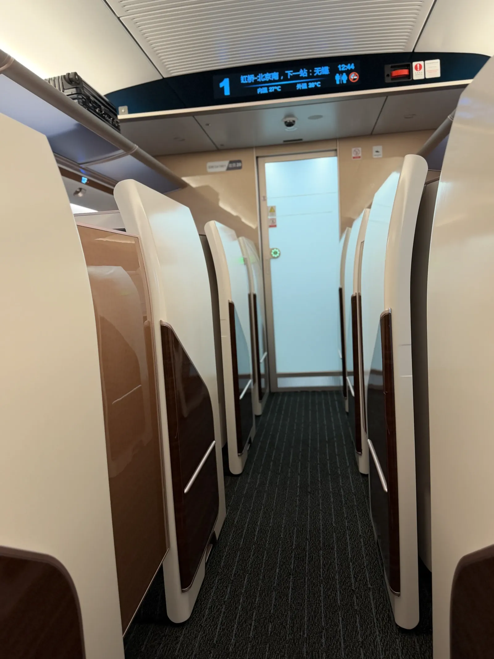 Leerer Gang im Business-Class-Wagen zwischen hohen Trennwänden, an der Decke eine Anzeige mit dem nächsten Halt