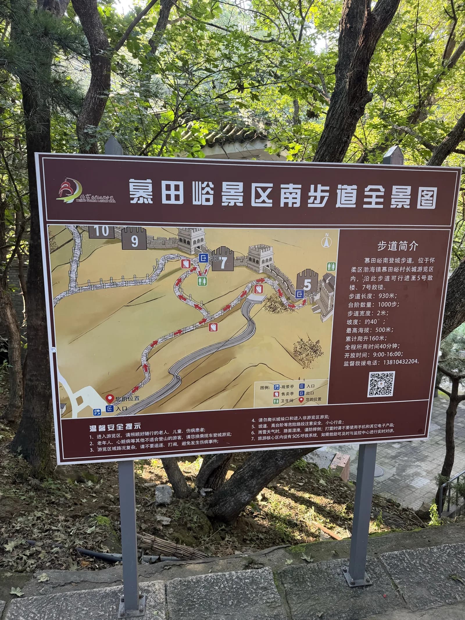 Braunes Informationsschild mit einer gezeichneten Karte der Mauer und chinesischem Text zum Fußweg, daneben Bäume