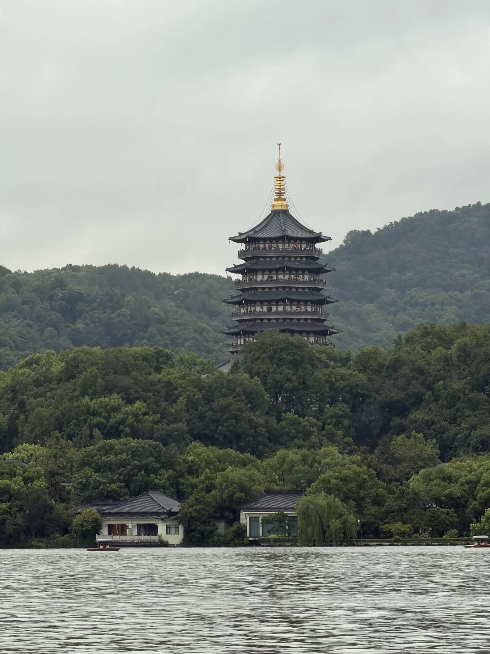 Die mehrstöckige Leifeng-Pagode mit goldener Spitze auf einem bewaldeten Hügel, davor der Westsee