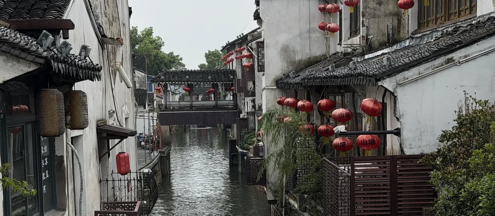 Kanal in der Altstadt von Suzhou mit weiß getünchten Häusern, roten Laternen und einer überdachten Brücke im Hintergrund