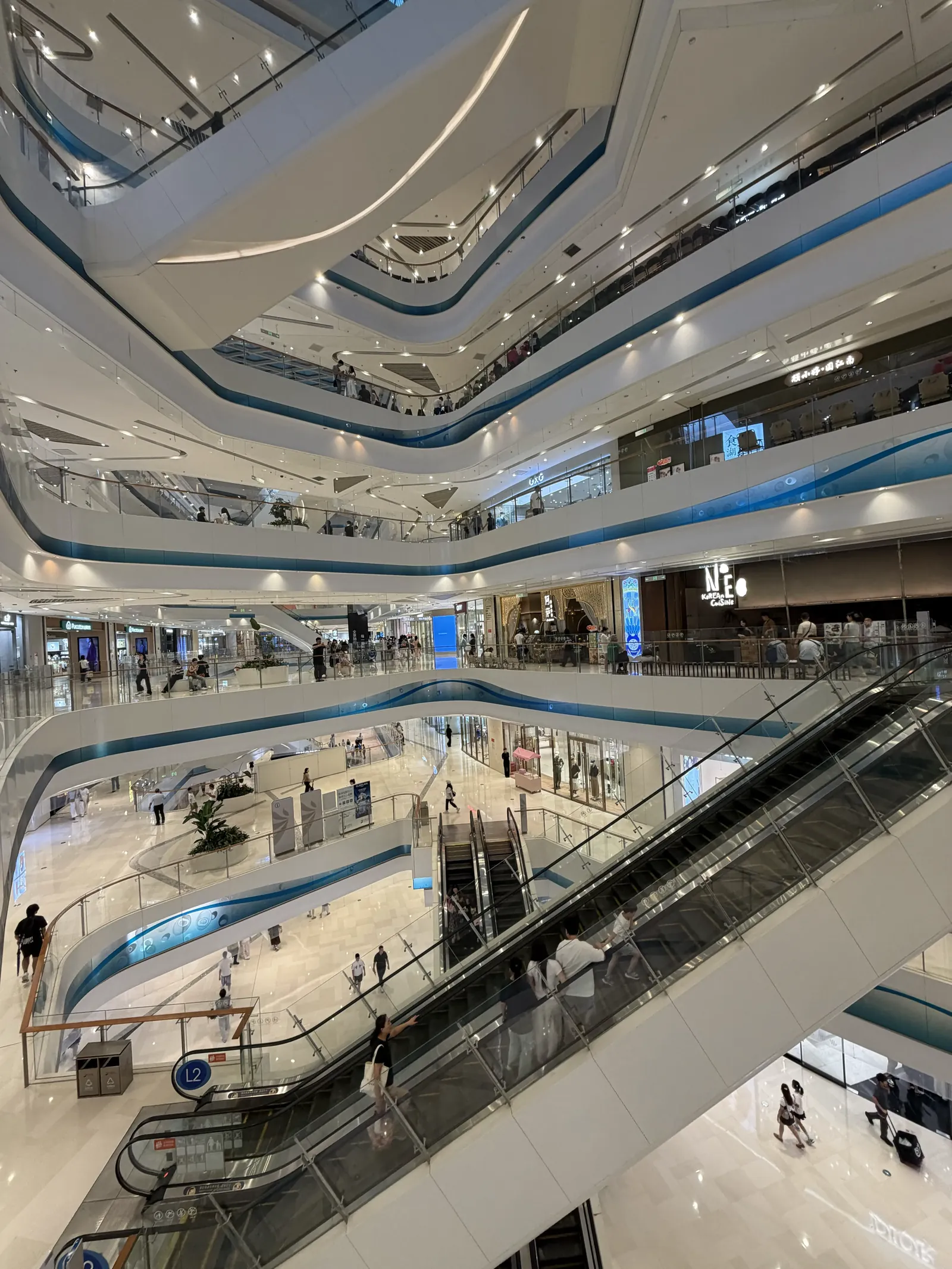Mehrstöckiges Atrium eines Einkaufszentrums mit geschwungenen weißen Galerien, Rolltreppen und Besuchern