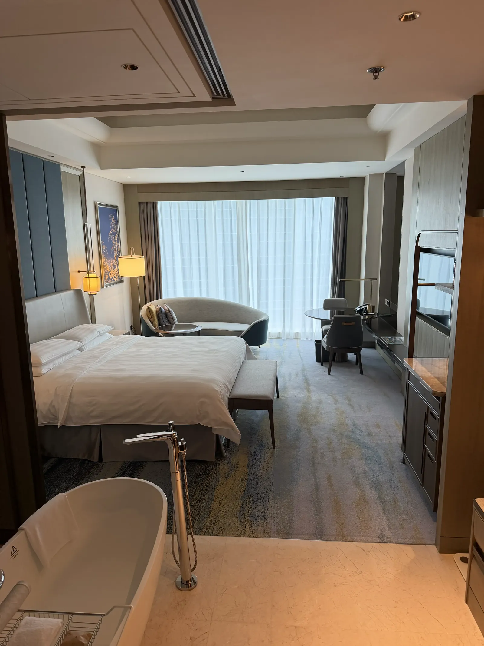 Hotelzimmer mit großem Bett, Sitzecke am bodentiefen Fenster und einer freistehenden Badewanne im Vordergrund