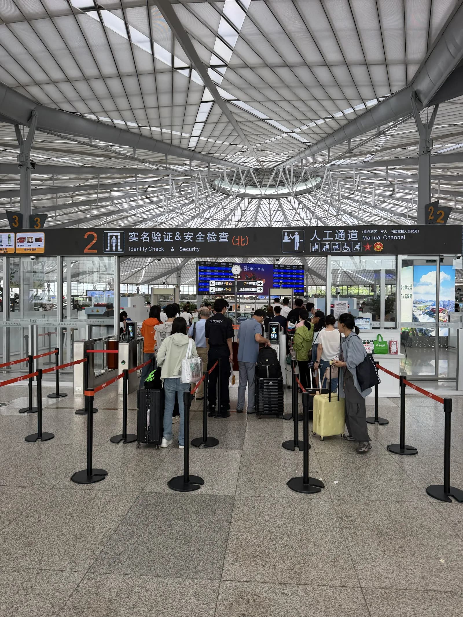 Identity Check und Security Gate im Shanghai South Bahnhof — Reisende mit Rollkoffern warten in einer Schlange vor den automatischen Turnstile-Geräten, rechts eine manuelle Spur mit Personal